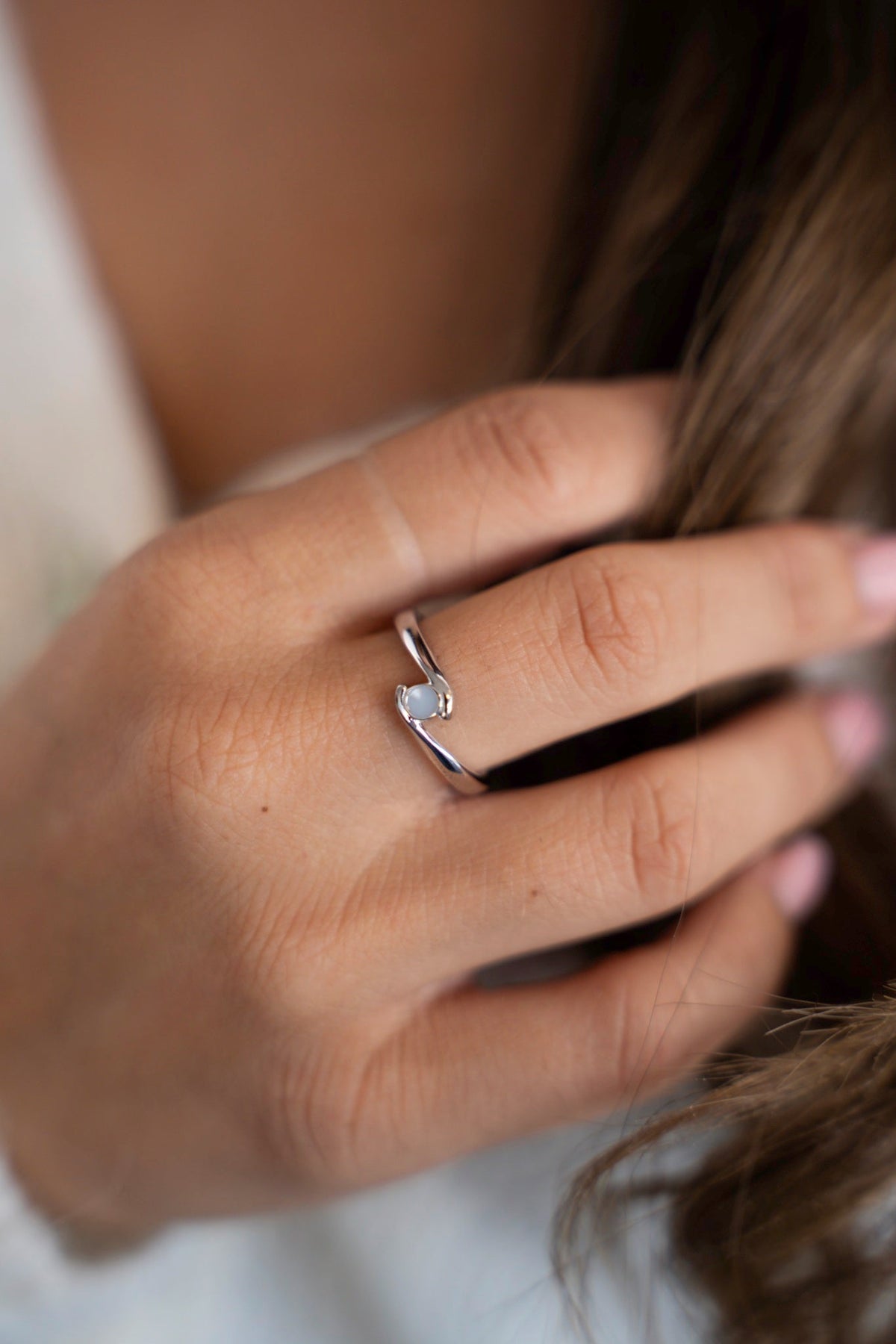 Bague au lait maternel Olivia en or blanc massif sur une main dans de longs cheveux ondulés.