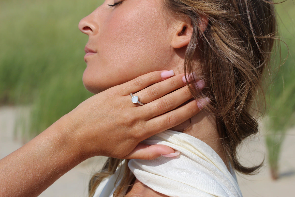 Main posée sur le cou portant la bague Turning Droplet avec goutte de lait maternel, dunes en fond